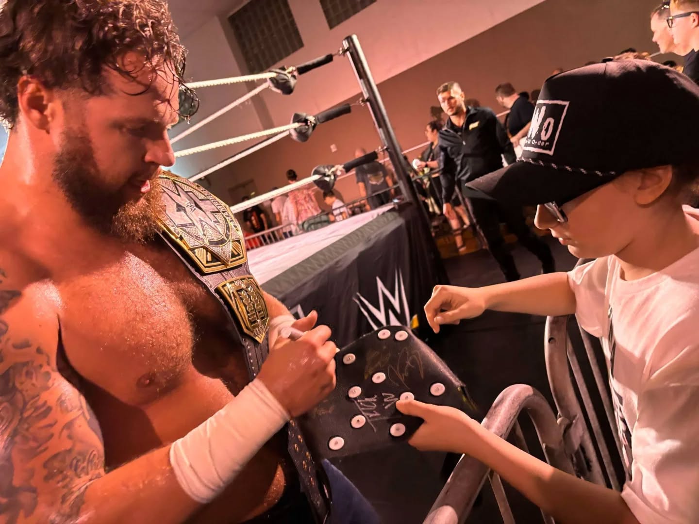 An NXT champion signs Trystan’s wrestling vest at ringside