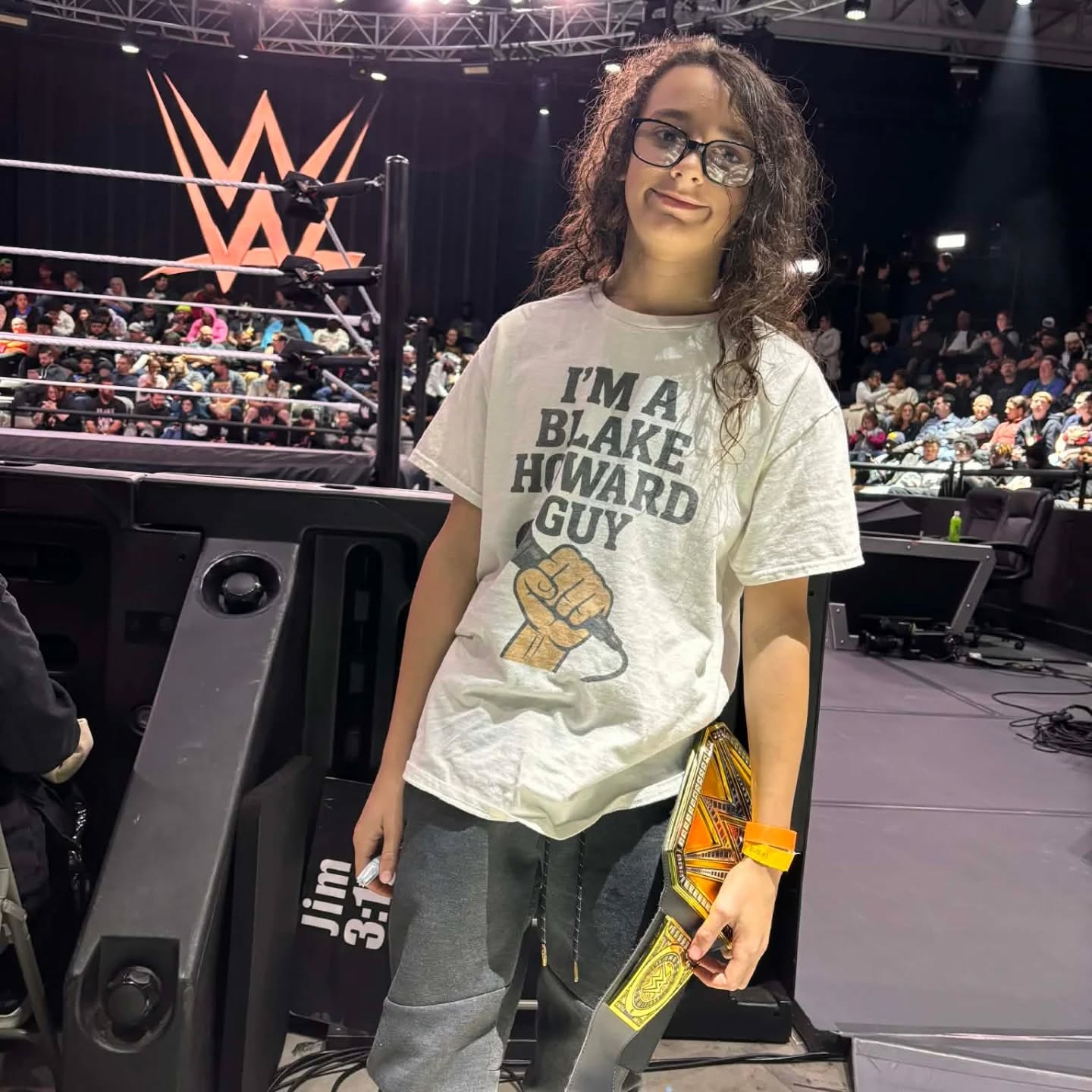 Trystan stands beside a WWE ring holding a championship belt